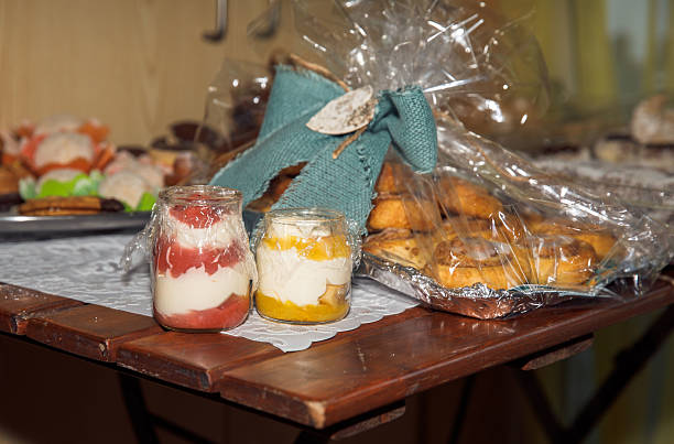 Assorted desserts on wooden table with fruit yogurt jars and wrapped pastries, lifestyle