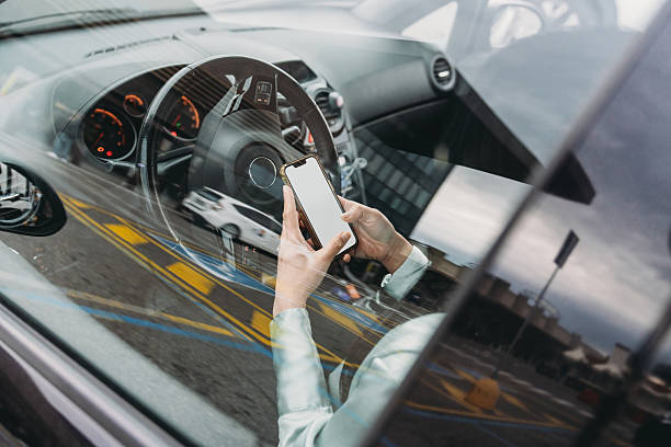 Businesswoman holding mobile phone with blank white screen while sitting in car, view through window