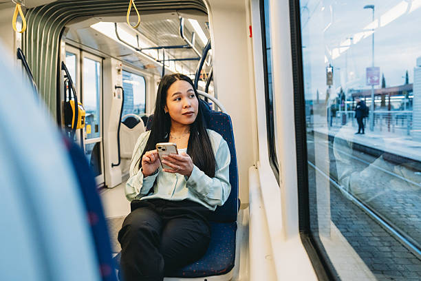 istock Young woman looking through the window while using her smartphone on the train 2211658589