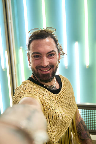 Latin transgender influencer taking a selfie with sunglasses and golden clothes Cheerful latin transgender influencer taking a selfie in sunglasses and golden clothes, surrounded by blurred blue and green neon lights gay man men sunglasses party stock pictures, royalty-free photos & images