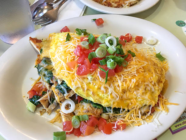 Delicious Ham and Cheese Omelette Garnished with Fresh Herbs on a Black Plate, Served with Tomato Sauce and Gold Cutlery, Breakfast Dish. Food and Lifestyle Concept