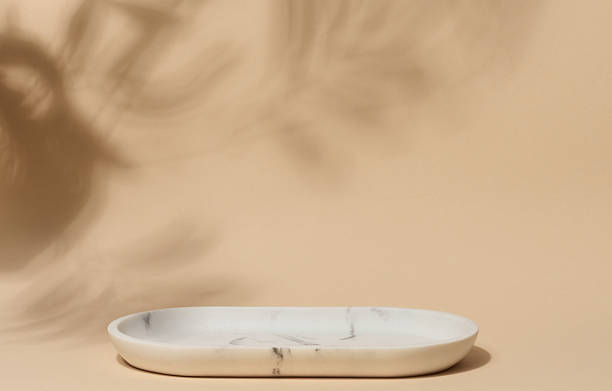 istock An empty, oval shaped soap dish made of white marble with gray veining sits on a beige background with soft, blurred leaf shadows 2211663925