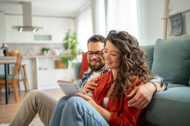 istock Young couple reading notes and embracing on living room floor 2211664321