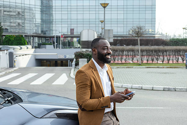istock Businessman leaning on car while using smartphone outdoors in modern urban environment 2211667947