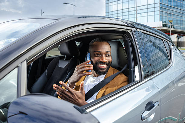 istock Smiling man talking on phone while sitting in parked car near modern building 2211668116