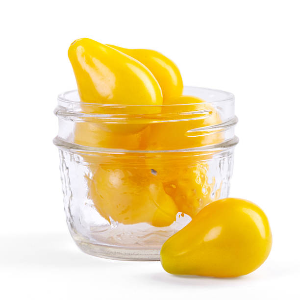 Yellow Pearshaped cherry tomatoes in a jar on white background.