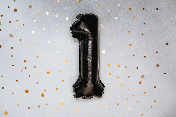 istock Black balloon number one on a shimmering golden confetti background 2211676780