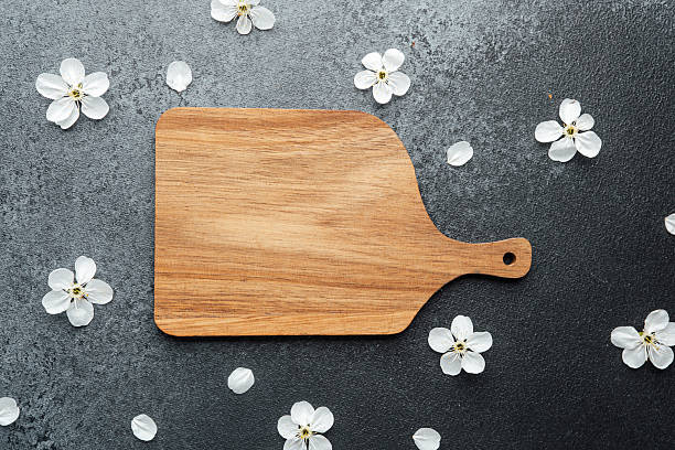 istock Wooden cutting board surrounded by delicate white flowers on a dark surface 2211676876