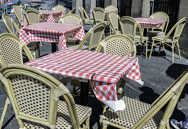 istock Empty tables and chairs covered red and white checkered tablecloths with chairs outside a cafe on street. 2211677315