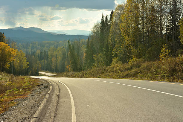 istock A wide two-lane paved road winds down a high mountain through a dense pine forest on a cloudy summer evening before sunset. 2211684719