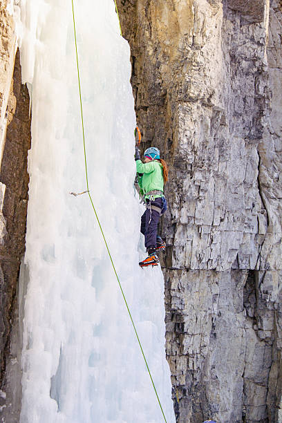 Canmore, Alberta Canada - January 22, 2022: A woman ice climbing a waterfall used for training beginner ice climbers at Grotto Canyon on a warm winter day.