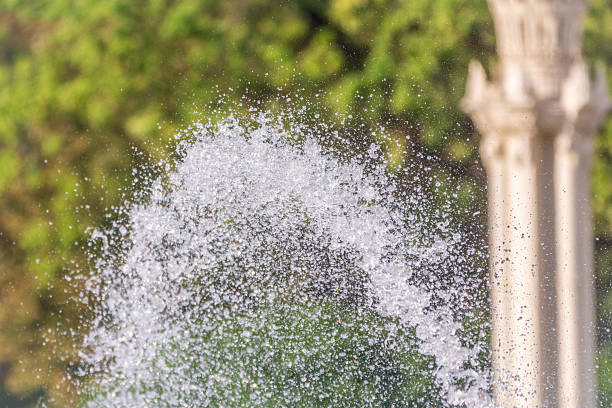Splashes of water against light background. Fountain, a jet of water against cloudy sky.
