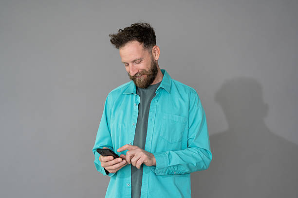 istock Happy smiling man using smart phone. Man writing a message with mobile isolated on gray background. 2211697793