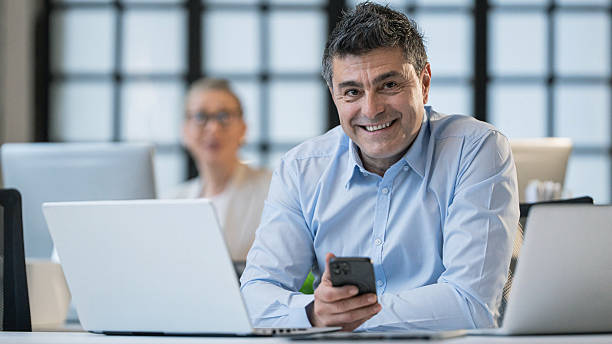 istock Man engaged with his smartphone and laptop in a modern office workspace setting. 2211707378