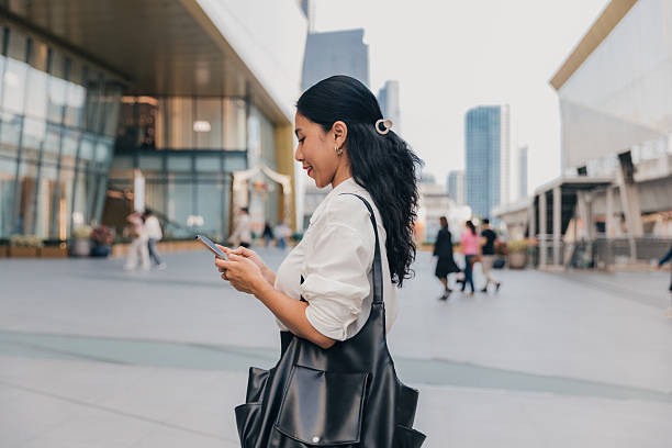 Young woman using smartphone in urban setting while walking past modern buildings during late afternoon
