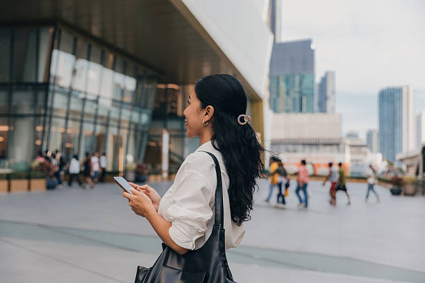 istock Woman using smartphone while walking in urban plaza with modern architecture and busy background 2211709354