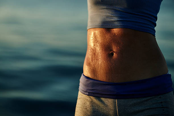 Close up of unrecognizable female athlete with sweaty abs in summer day on the beach. Copy space.