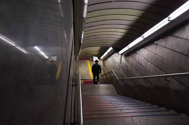 Busan, South Korea - March 19, 2018: A person walks down a staircase in a dimly lit metro underpass, accentuating solitude and urban travel