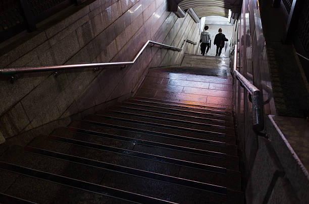 Busan, South Korea - March 19, 2018: Dimly lit subway stairs lead to an exit as two individuals walk down under soft lighting
