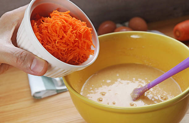 istock Hand adding shredded carrot into the mixing bowl of batter for baking cake 2211719137