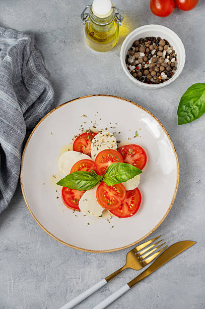 istock Caprese salad with sliced tomatoes, mozzarella and basil on a plate on a light background 2211720412