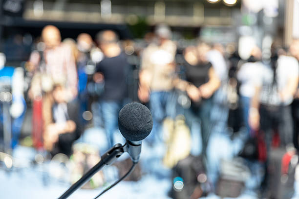 istock Microphone in focus at media event, press or news conference, blurred video camera operators in the background 2211721603
