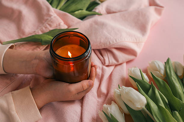 istock Hands gently holding a lit candle over a pink denim jacket, surrounded by fresh white tulips on a soft pink background, evoking calmness and warmth 2211721675