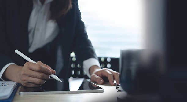 istock Closeup, Businesswoman using digital tablet, working at modern office. Business woman using stylus pen signing, proofing e-document on touchpad on office table, e-signing, business planning 2211722471