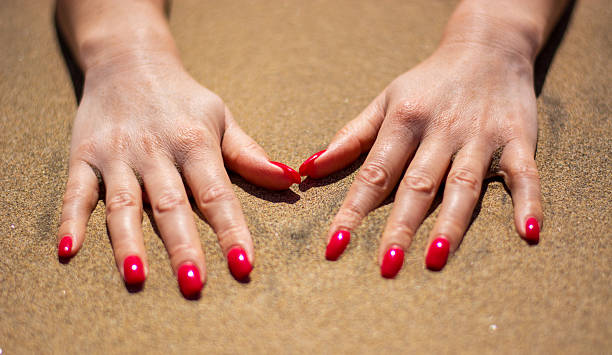 istock a woman's hands with red nails in the sea sand 2211724550