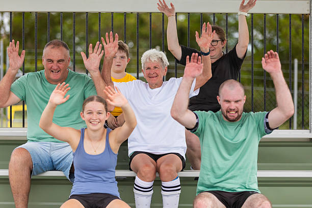 Happy smiling sporty group of people jumping standing in a circle in nature with hands up rejoicing the success in sport training or exercise achievement outdoors after workout in the park.