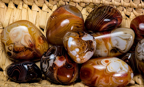A variety of polished agate stones with diverse patterns and colors, including brown, white, orange, and black, are nestled within a textured woven basket