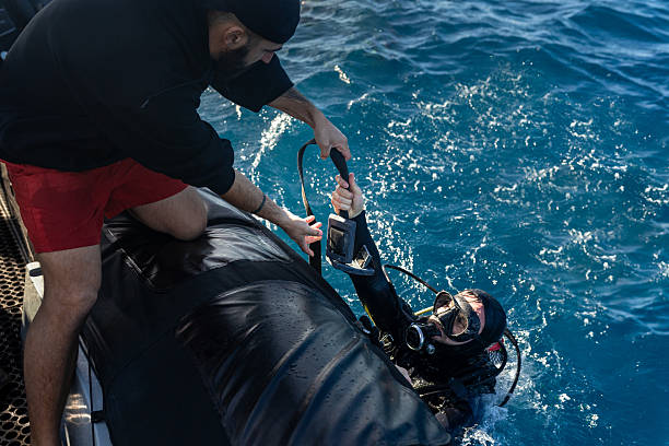 Scuba diver holding a rope being helped by sailor to climb back on inflatable boat after a dive
