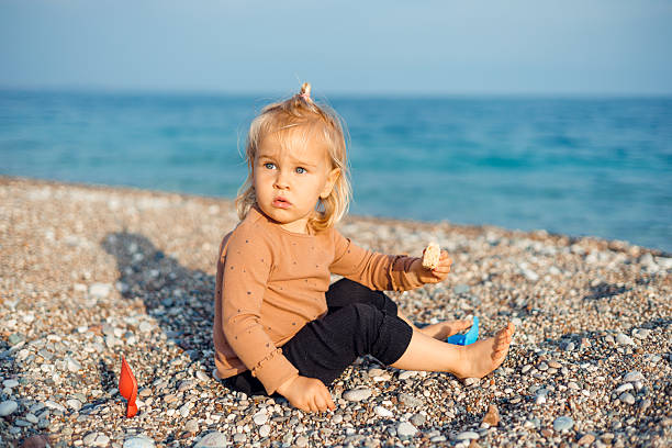 istock Toddler enjoys a snack while playing on a pebble beach near the ocean 2211741882