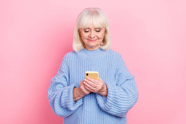 istock Portrait of attractive focused grey-haired woman using device chatting smm post isolated over pink pastel color background 2211745822