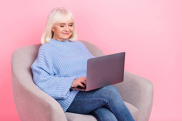 istock Portrait of attractive focused grey-haired woman using laptop writing e-mail isolated over pink pastel color background 2211745916