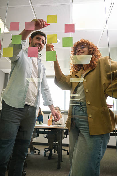 istock Young professionals organizing notes on glass wall in office 2211747471