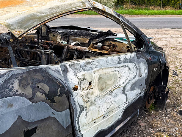 istock Side view of a completely burned car showing warped and blistered paint, missing interior, and rusted components after an intense fire incident near a roadside 2211759483