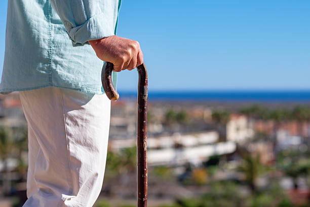 Senior caucasian man with back problems walking with the help of a cane. Elderly people outdoor face the sea, horizon over water