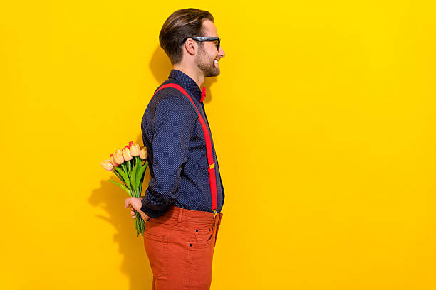 istock Profile side photo of young cheerful man look empty space hide bouquet behind back isolated over yellow color background 2211761212