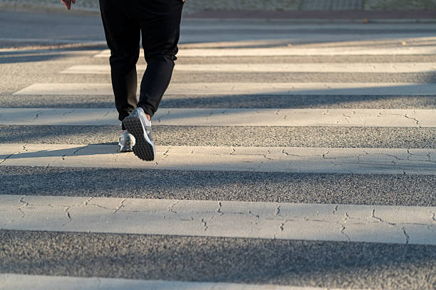 istock Individual Walking on Crosswalk During Daylight Hours With Shadow Patterns on Pavement 2211762148