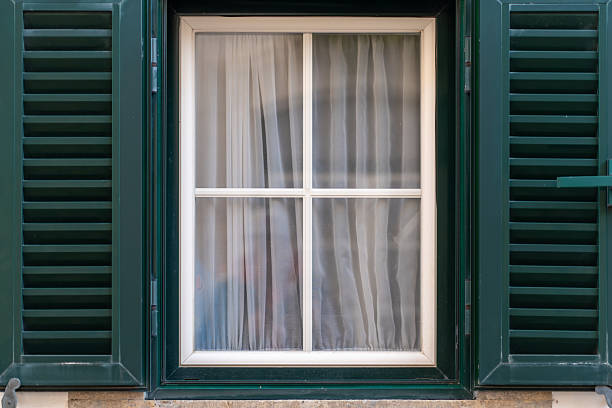 Elegant Window With Closed Green Shutters and Sheer Curtains in a Quaint Building