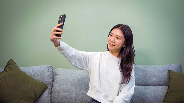 istock Smiling young woman taking a selfie with phone on home sofa 2211763012