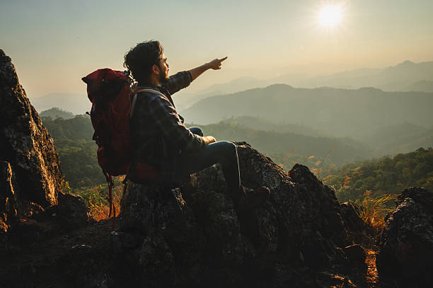 istock man with a backpack is sitting on a rock and pointing to the sky 2211769108