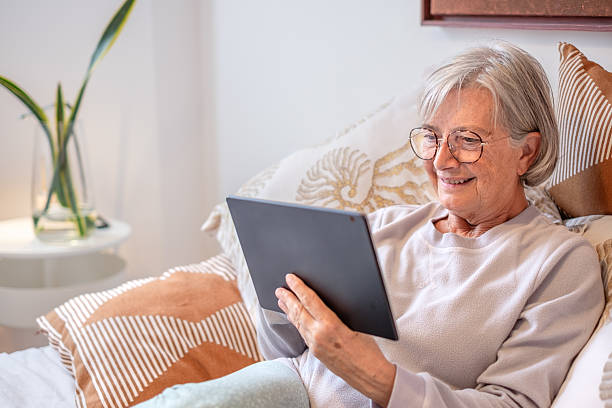 istock Smiling relaxed senior woman lying in bed using a digital tablet communicating in remote chat with family or browsing internet 2211770094
