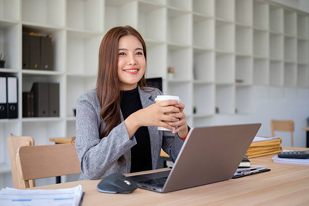 istock Smiling businesswoman enjoying coffee while working on laptop in modern office. 2211776516