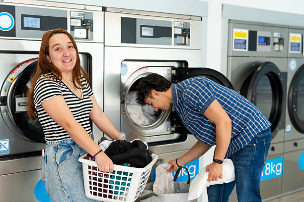 istock Young couple doing laundry at laundromat: washing clothes together 2211780868