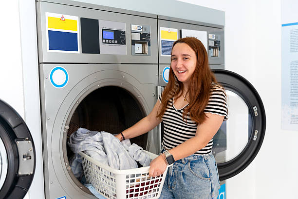 istock Young woman loading clothes into washing machine at laundromat 2211780897