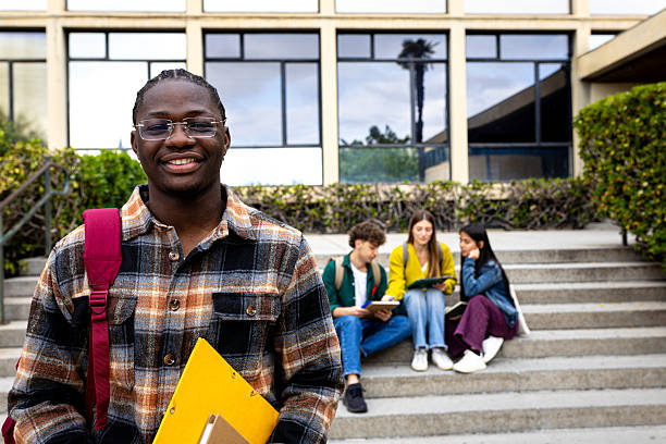 istock Smiling university student standing with books and backpack in front of university building 2211782296