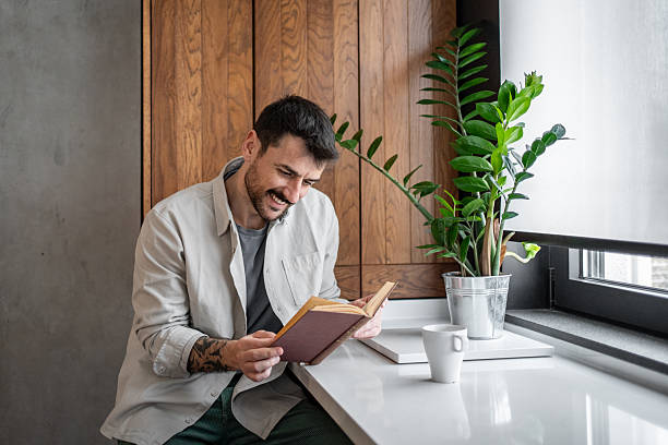 istock Young man enjoying a book with coffee in modern kitchen 2211782940