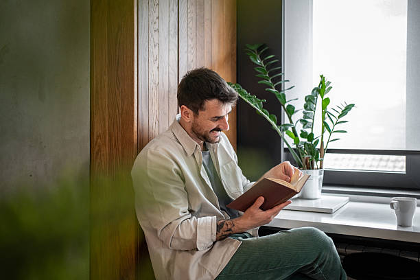 istock Smiling man reading a book by the window 2211783647